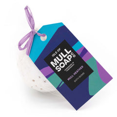 white coloured round mull heather bath bomb presented as a gift in a bag with coloured tag and bow. decorated with heather flowers. Handmade by the Isle of Mull soap co in Tobermory, Scotland.