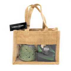 A natural coloured jute bag gift set with front window. Contains a green leaf and flower cut out ceramic burner and 2 Alien perfume scented soy wax melt snap bars made by the Isle of Mull soap co in Tobermory. contains packing shred and handles tied with a black tag.
