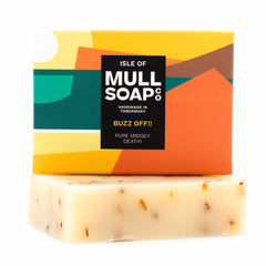 a buzz off insect repellent soap box sitting on top of the soap bar. The box is bright orange green and yellow and says 'pure midget death' Handmade in Tobermory by the Isle of Mull soap co.