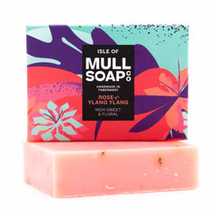 a rose and ylang ylang soap box sitting on the pink soap bar. The box is a pink and purple colourful floral design. The soap is described as rich, sweet and floral. Handmade in Tobermory by the Isle of Mull soap co.