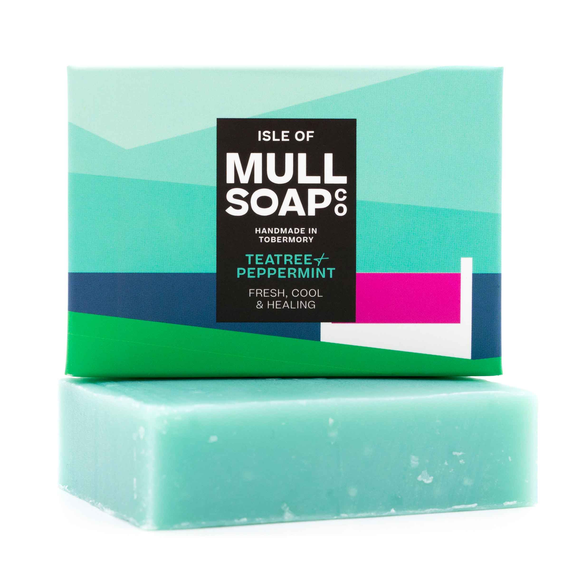 a Teatree and peppermint soap box sitting on the blue soap bar. The box is a sea landscape with a pink roofed cottage. The soap is described as fresh, cool and healing. Handmade in Tobermory by the Isle of Mull soap co.