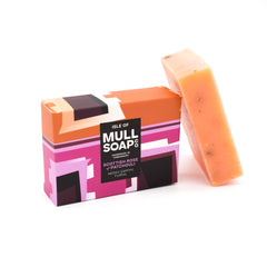 a Scottish rose and patchouli soap box sitting next to the pink soap bar. The box is a pink colourful design. The soap is described as mossy, earthy and floral. Handmade in Tobermory by the Isle of Mull soap co.